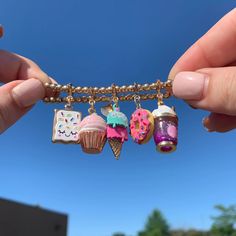 a hand holding a chain with charms attached to it that have cupcakes and donuts on them