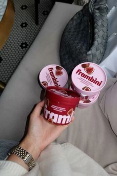 two yogurts are being held up by someone's hand while sitting on a couch