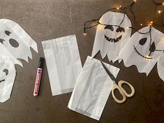 paper bags with ghost faces cut out and scissors on the ground next to them, along with string lights