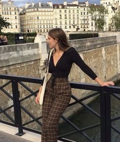 a woman is standing on a bridge with her hands in her pockets and looking at the camera