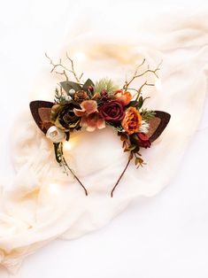 a cat ears headband with flowers and leaves on top of a white cloth background