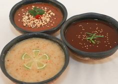 three bowls filled with different types of soups and sauces on top of a white table