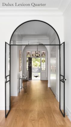 an arched glass door leading to a hallway with hardwood floors and white walls, along with a chandelier hanging from the ceiling