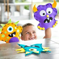 a young boy sitting at a table next to two stuffed animals that look like monsters