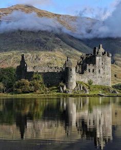 a castle sitting on top of a lush green hillside next to a body of water