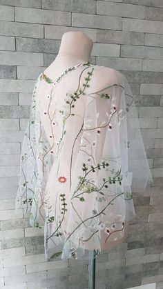 the back of a dress with flowers and leaves on it, sitting on a mannequin