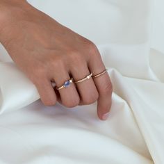 a woman's hand with two gold rings on top of white sheets and the other one has a blue diamond