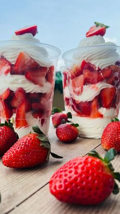 strawberries and whipped cream in plastic cups on wooden table with blue sky behind them