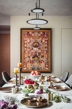 a dining room table is set with plates and flowers, candles, and an embroidered wall hanging