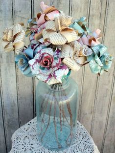 a vase filled with lots of paper flowers on top of a doily covered table