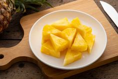 sliced pineapple on a white plate next to a knife and cutting board with cut pineapple