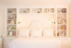 a bed with white linens and pillows in a room that has shelving on the wall