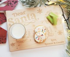 a wooden cutting board topped with cookies next to a glass of milk and christmas decorations