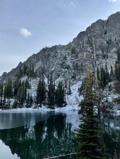 the mountain is covered in snow and surrounded by pine trees, with a lake below it