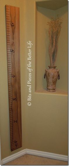 a tall wooden ruler next to a wall with a vase on it's side