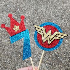 two cake toppers made to look like superman and wonder woman logos on toothpicks