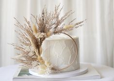 a white cake sitting on top of a table next to a book and some dried plants