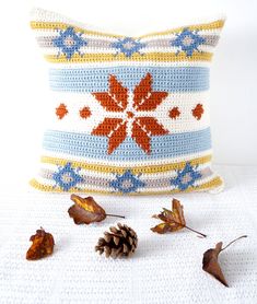 a crocheted pillow with pine cones and leaves on the ground next to it