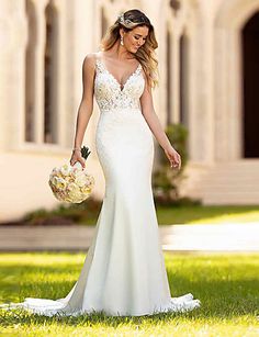 a woman in a white wedding dress walking through the grass with flowers on her hand