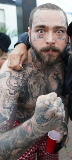 a man with tattoos on his face and arm is hugging another man's shoulder