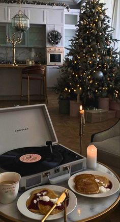 a christmas tree is in the background behind a suitcase with pancakes and coffee on it