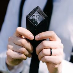 the man is holding up his wedding photo in front of him and he has an engagement ring on his finger