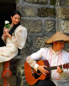 a man with a guitar and a woman wearing a hat sitting on a stone wall