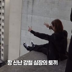 a woman sitting on top of a cement wall with her hands out in the air