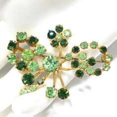 *Description: This is a beautiful green rhinestone brooch, made in Austria, from the 1950s. The rhinestones are in two shades of green; peridot green and emerald green, on a gold tone background. All of the Austrian brooches have exquisite rhinestones. This would be a great addition to your vintage jewelry collection or make a great vintage gift! *Approximate Measurements: Length - 1 1/2 Inches, Width - 2 1/8 Inches, Weight - .3 Ounce *Condition: Great vintage condition. Pin in clasp is brass an Antique Green Brooch For Evening, Mid-century Green Brooch For Formal Occasions, Mid-century Green Brooches For Formal Occasions, Antique Green Brooch For Anniversary, Vintage Green Brooch For Evening, Antique Green Brooches For Anniversary, Vintage Green Evening Brooch, Vintage Green Evening Brooches, Green Mid-century Style Brooches For Formal Occasions