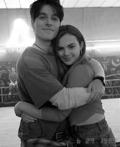 a man and woman hugging each other in front of a wall