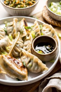 a white plate topped with dumplings next to a bowl of salad and dipping sauce