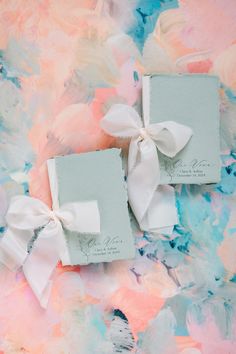 two small white boxes with bows on them sitting on a pink and blue floral background