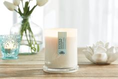 a white candle sitting on top of a wooden table next to a vase with flowers