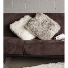 two pillows sitting on top of a brown couch next to a white rug and a brick wall