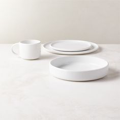 three white plates and two cups sitting on top of a table with no one around them