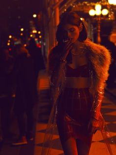 a woman walking down the street at night with her cell phone to her ear and wearing a fur coat