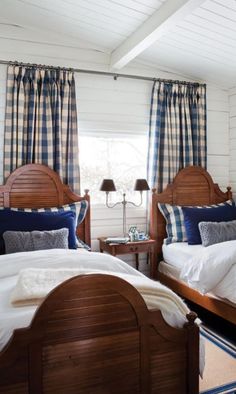 two twin beds in a bedroom with blue and white bedding, plaid curtains, and wooden headboards