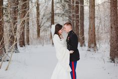 a bride and groom are standing in the snow near some trees with their arms around each other