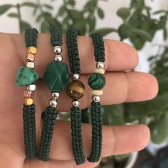 two green bracelets with beads and stones on them, sitting in front of a potted plant