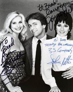 two women and a man posing for a photo with autographs on the wall behind them