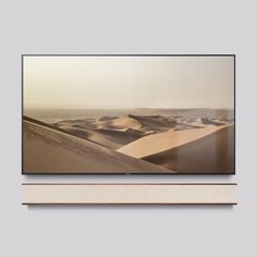 a flat screen tv mounted on a wall in front of a shelf with an image of sand dunes