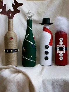 three wine bottles decorated with christmas decorations on a white cloth covered tablecloth, one has a snowman and the other is a reindeer