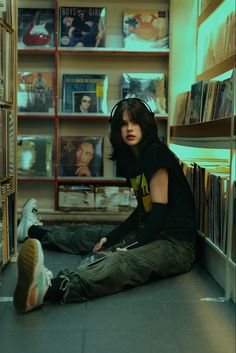 a woman sitting on the floor in front of a book shelf filled with books and cds