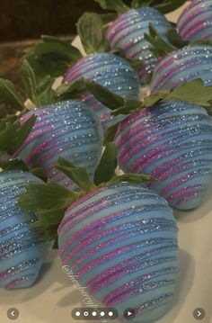 blue and pink striped strawberries on a white platter with green leaves around them