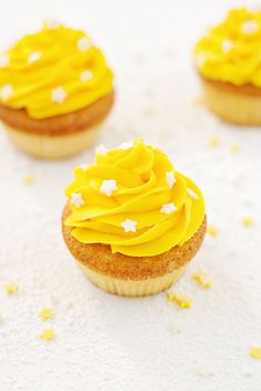 three cupcakes with yellow frosting and white sprinkles on top