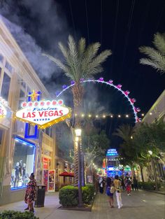 the las vegas sign is lit up at night with palm trees and people walking down the street