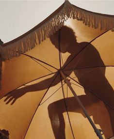 the shadow of a person standing under an umbrella with fringe trimmings on it