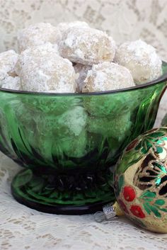 a green glass bowl filled with powdered sugar covered cookies next to an ornament