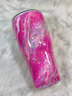 a pink and purple tumbler sitting on top of a white fur covered floor with lots of glitter