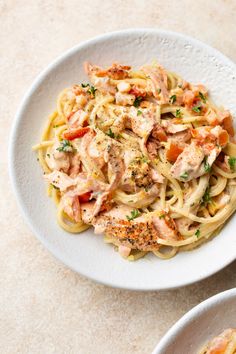 two white bowls filled with pasta covered in chicken and sauce on top of a table